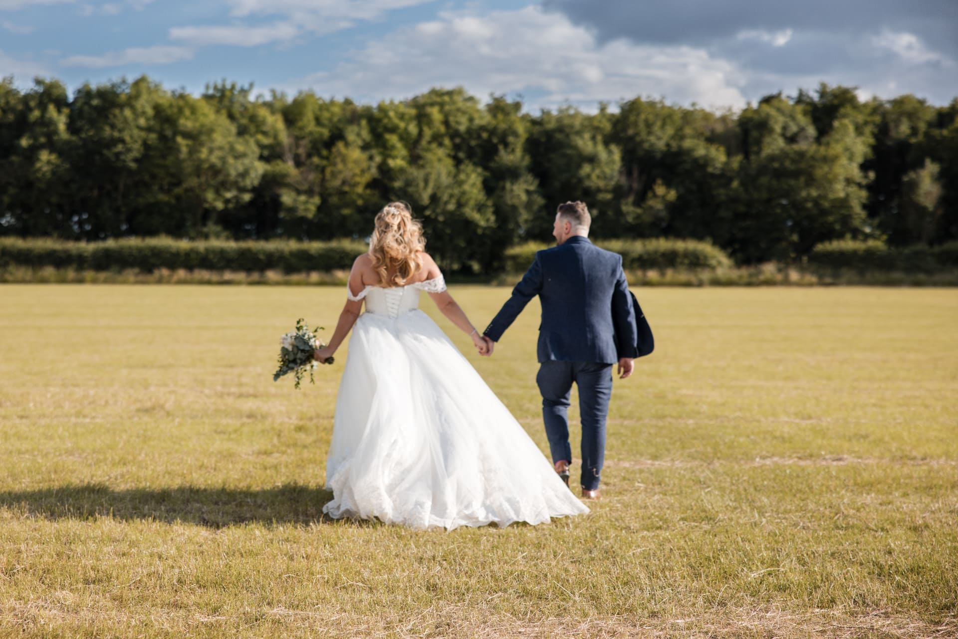 bride and groom walking away across field