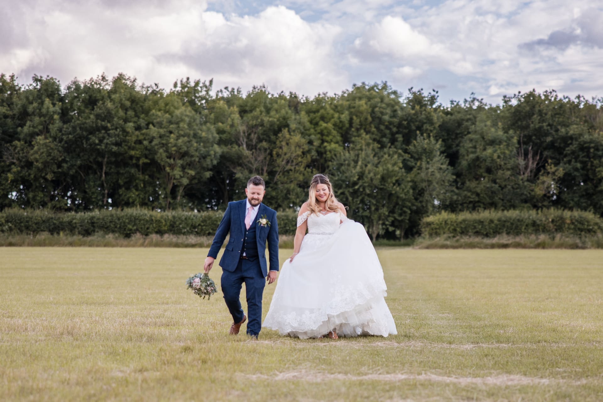 bride and groom walking towards camera in field