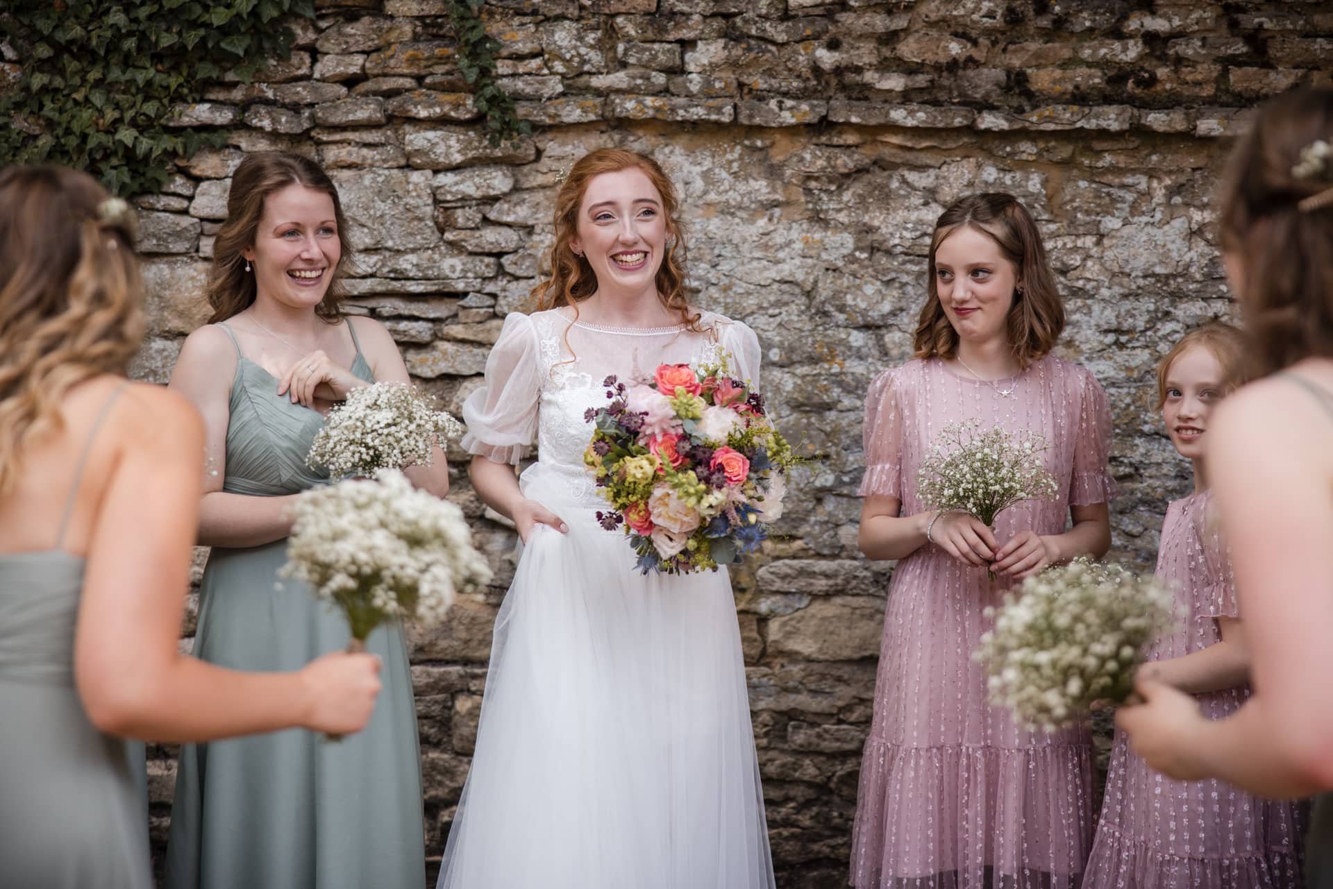 Bride relaxing with Bridesmaids with cotswold stone wall behind them