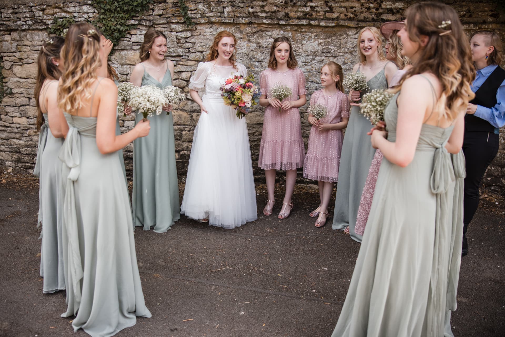 Bride is surrounded by her bridesmaids against the Cotswold stone wall