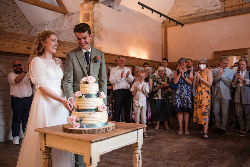 Bride and Groom cutting of the wedding cake with guests onlooking