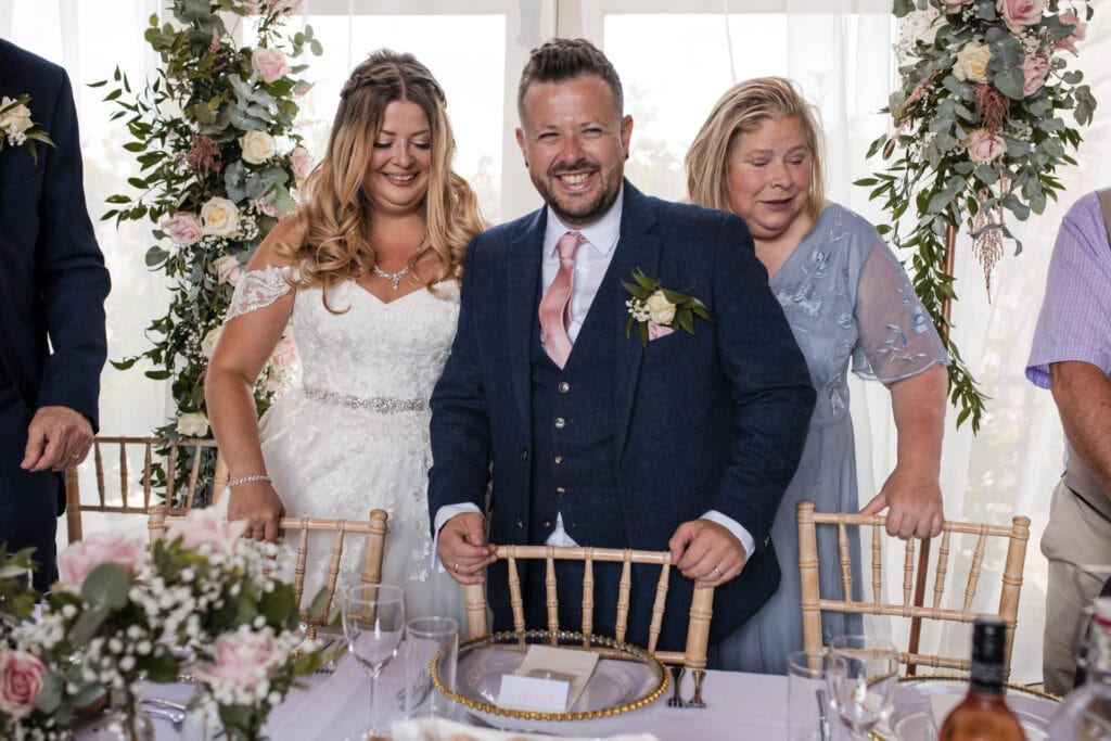 Bride and Groom about to sit at wedding reception at Stratton Court Barn Wedding Venue
