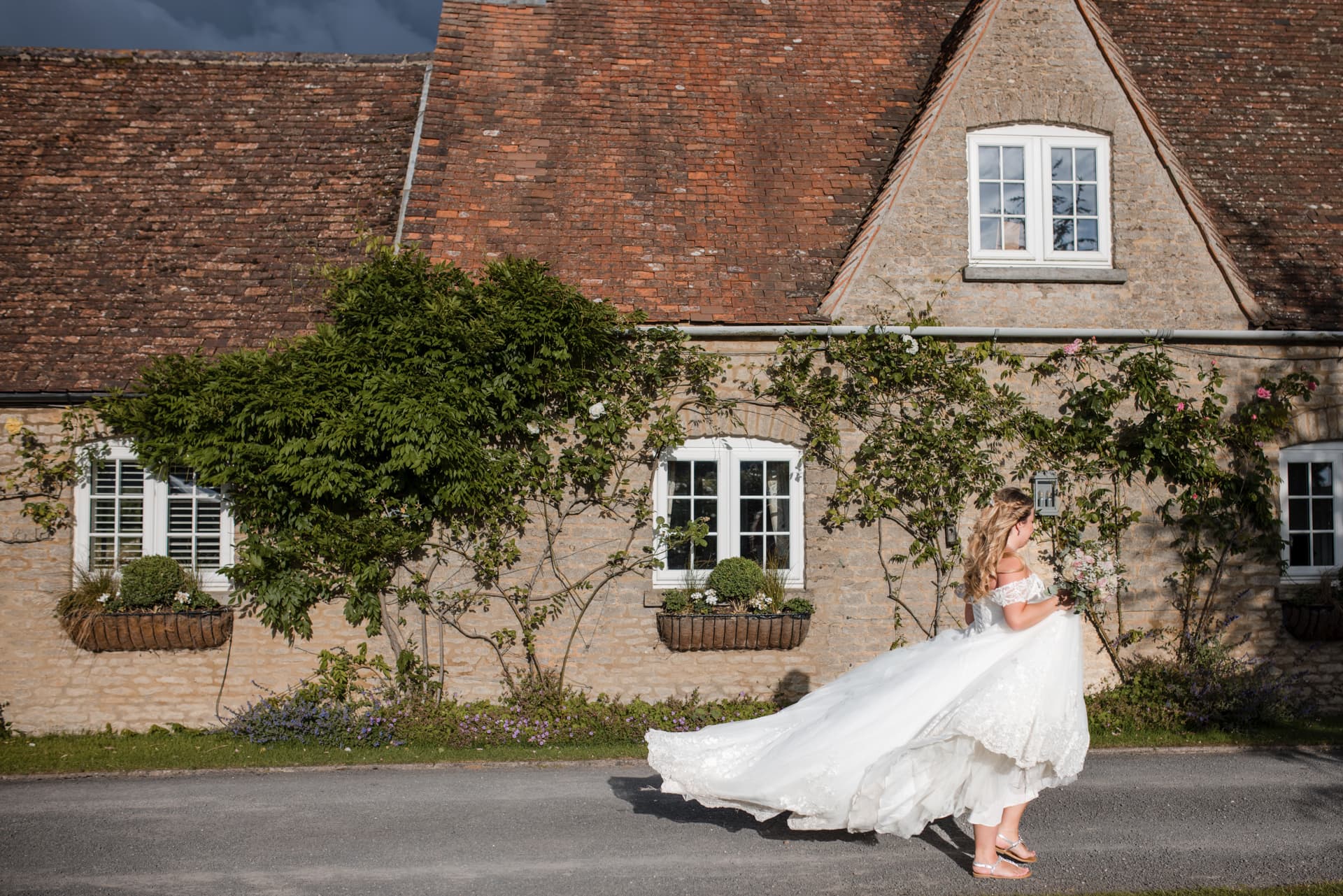 Bride walking in front of old cottage farmhouse at the Stratton Court Barn Wedding Venue