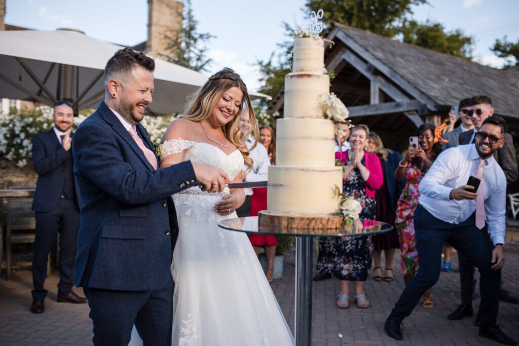 Cutting the wedding cake in the Courtyard of Stratton Court Barn Wedding Venue