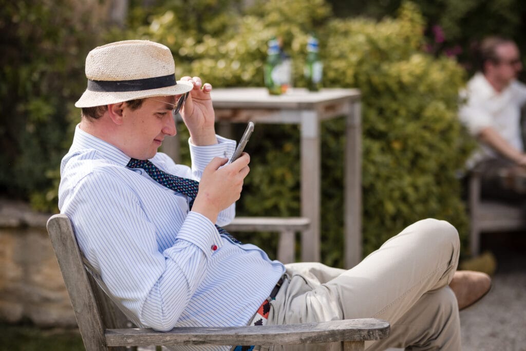 Gentleman in hat looking at phone in the garden of Oxleaze Barn