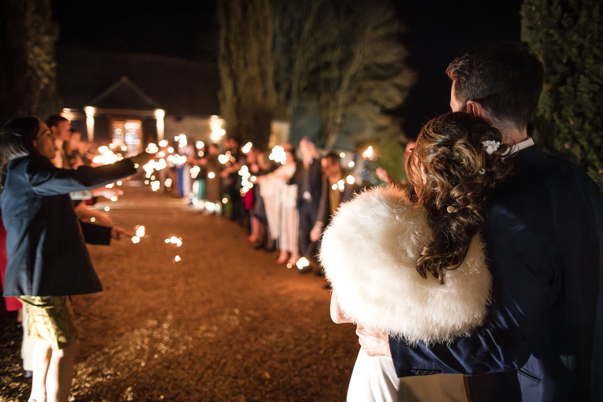 Wedding couple looking on at guests during sparklers outside of Notley Barn