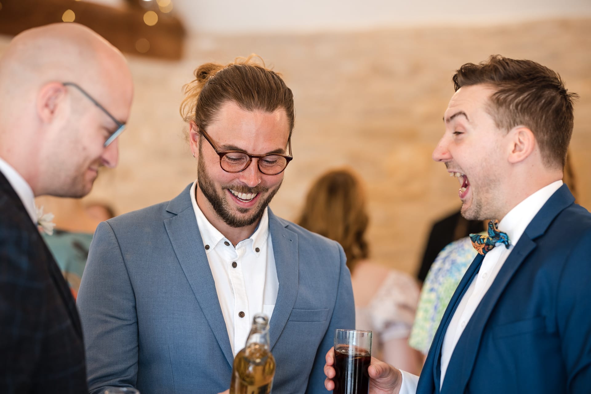 Weddings guests laughing over a drink at Kingscote Barn