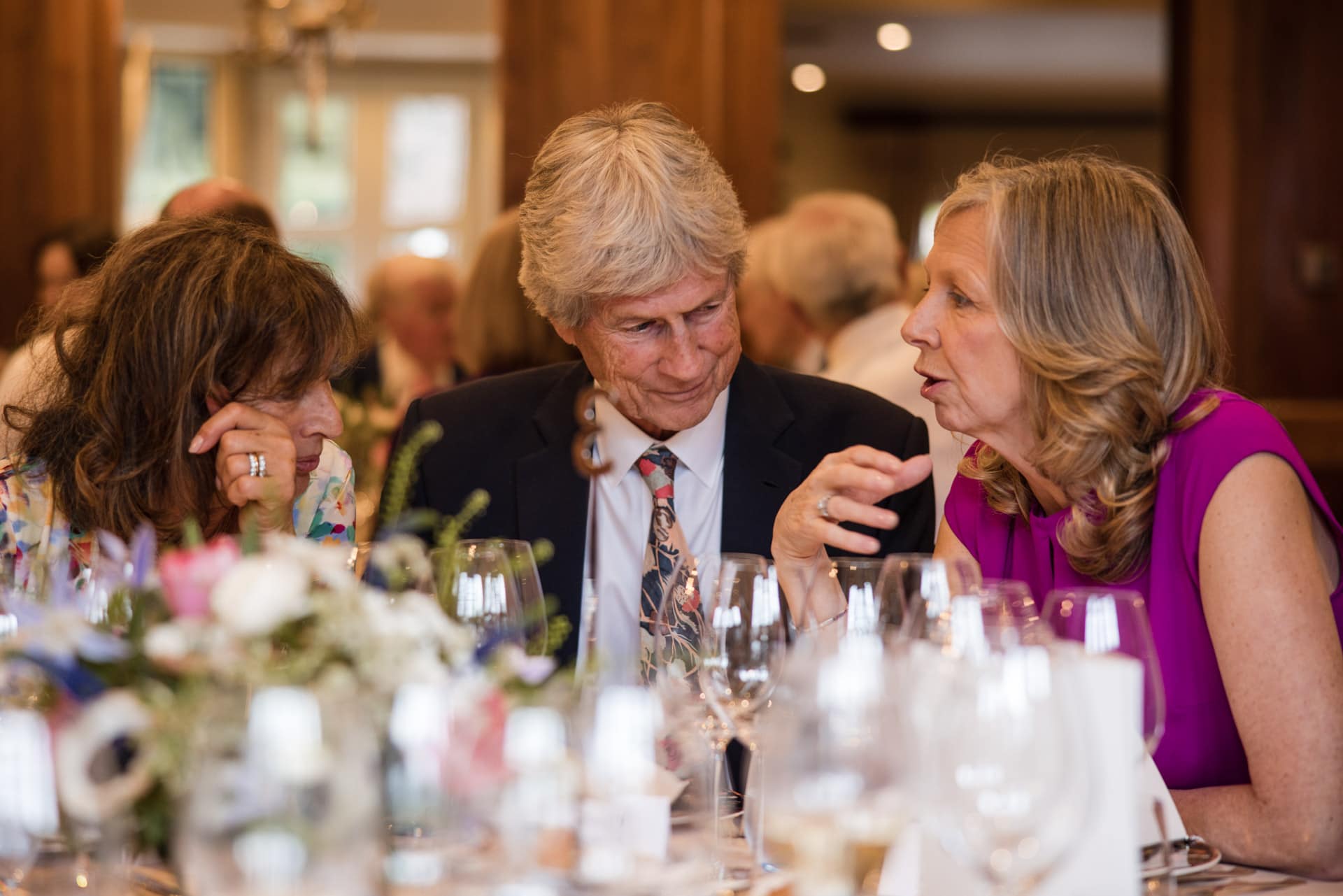 Two female guests chatting across a male guest at the wedding breakfast