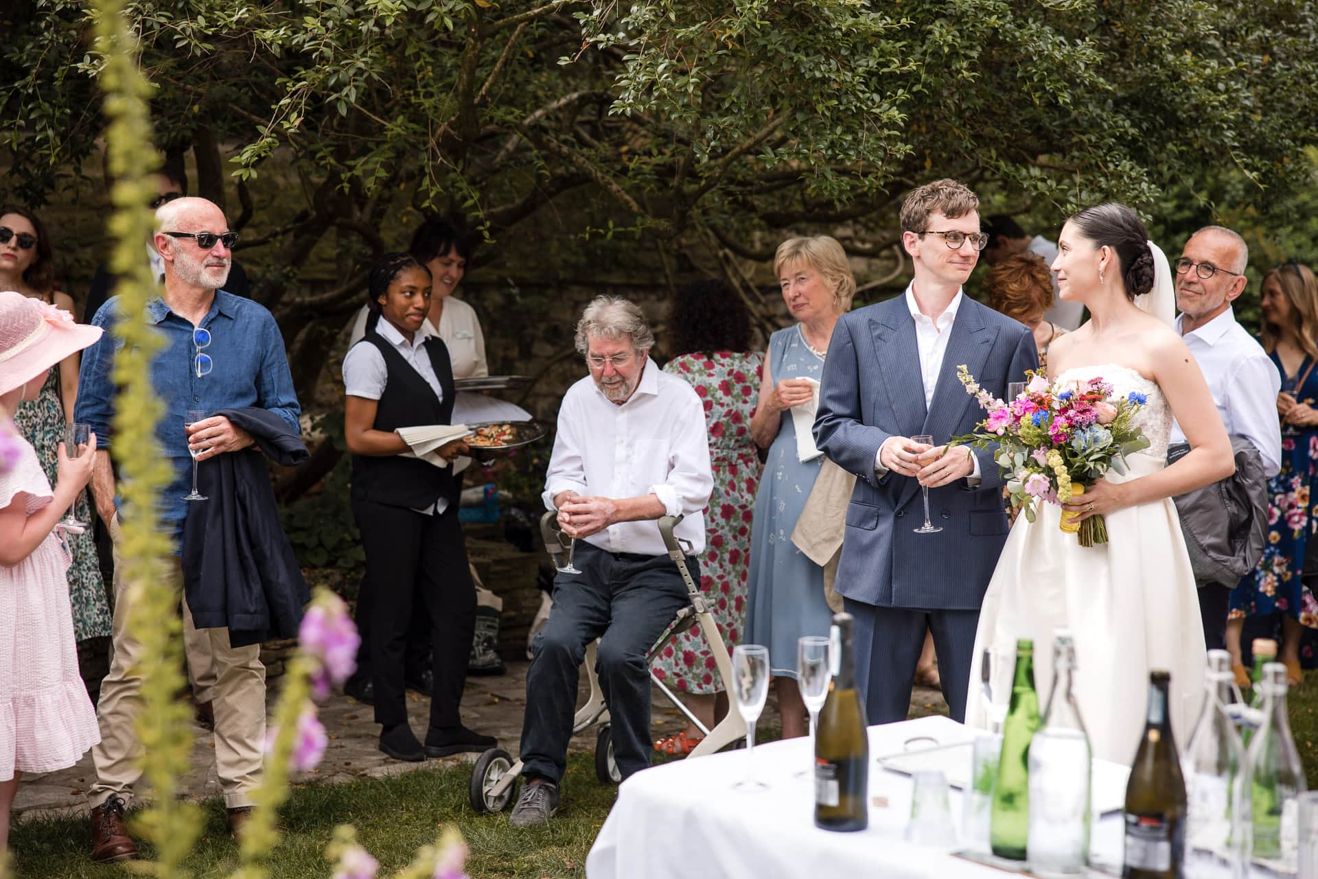Bride and Groom drinking Champagne surrounded by guests in the Masters Garden at Pembroke College