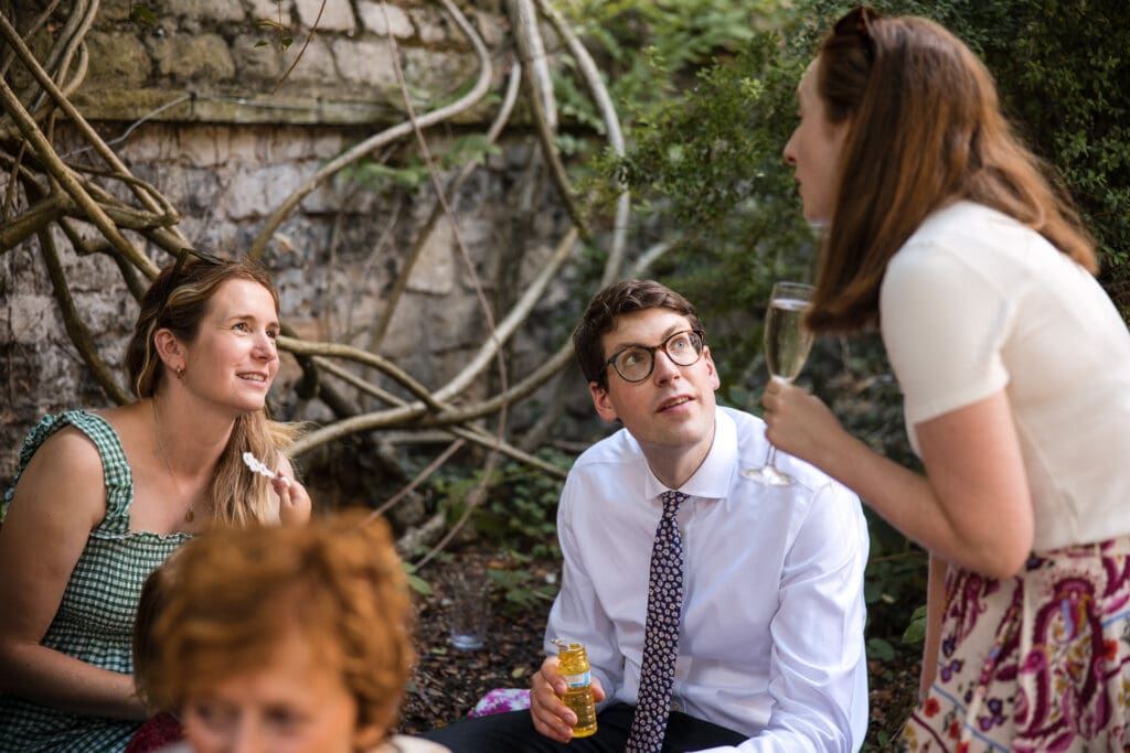 Two seated guests chatting to another guest in the Masters Garden at Pembroke College.