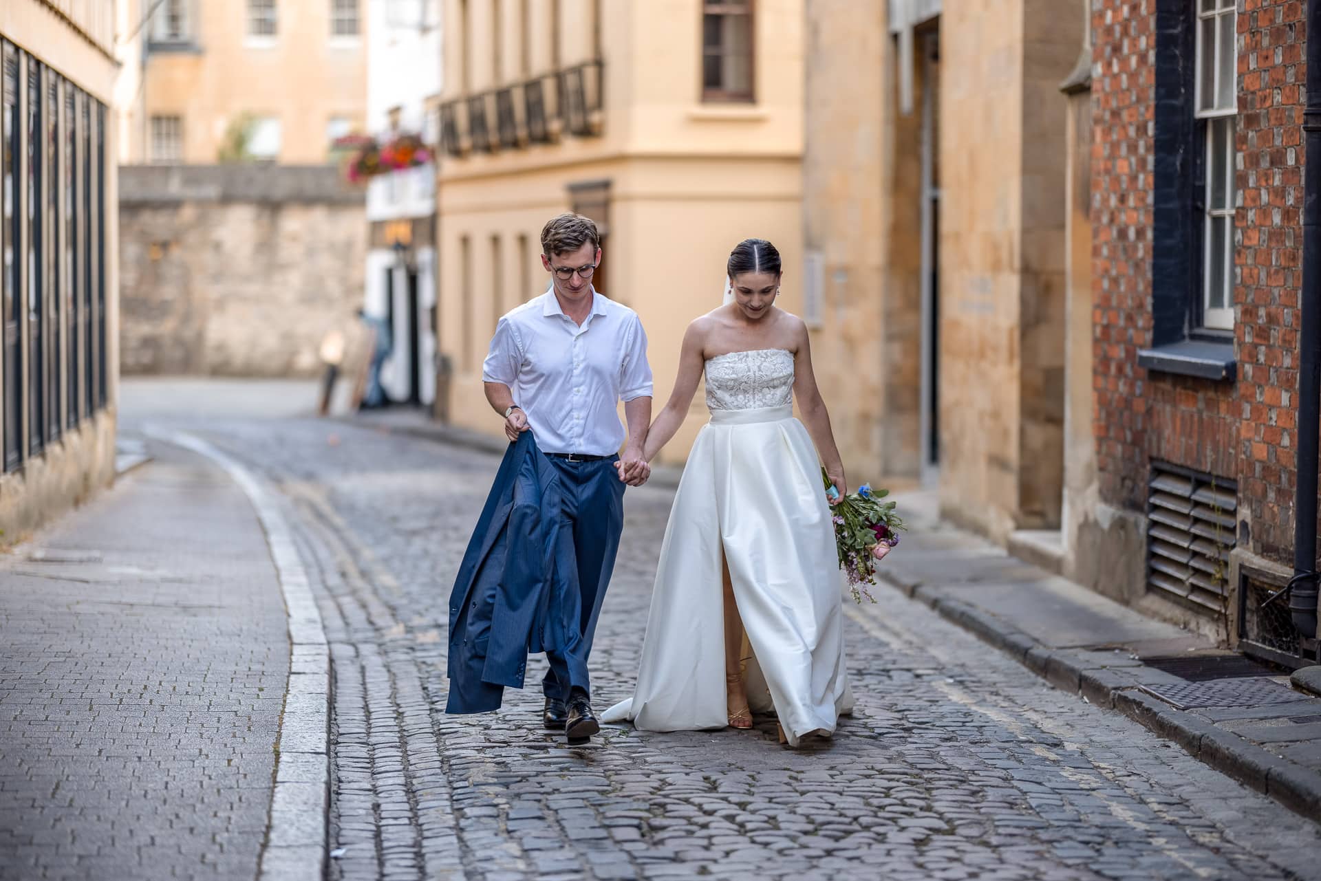 The Bride and Groom walking hand in hand on a cobbled street in Oxford.