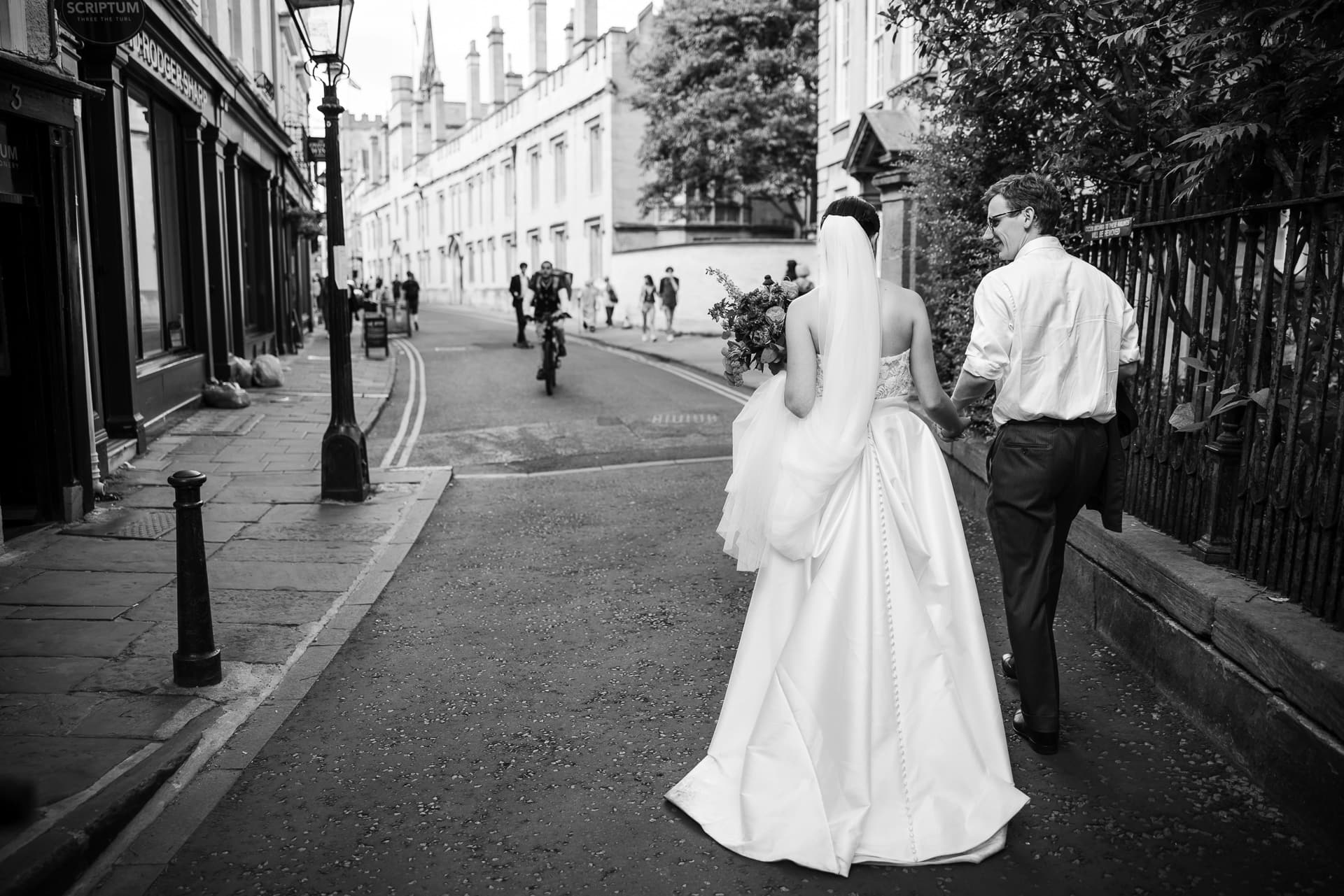 A view from behind of the bride and groom as they walk down the street in Oxford