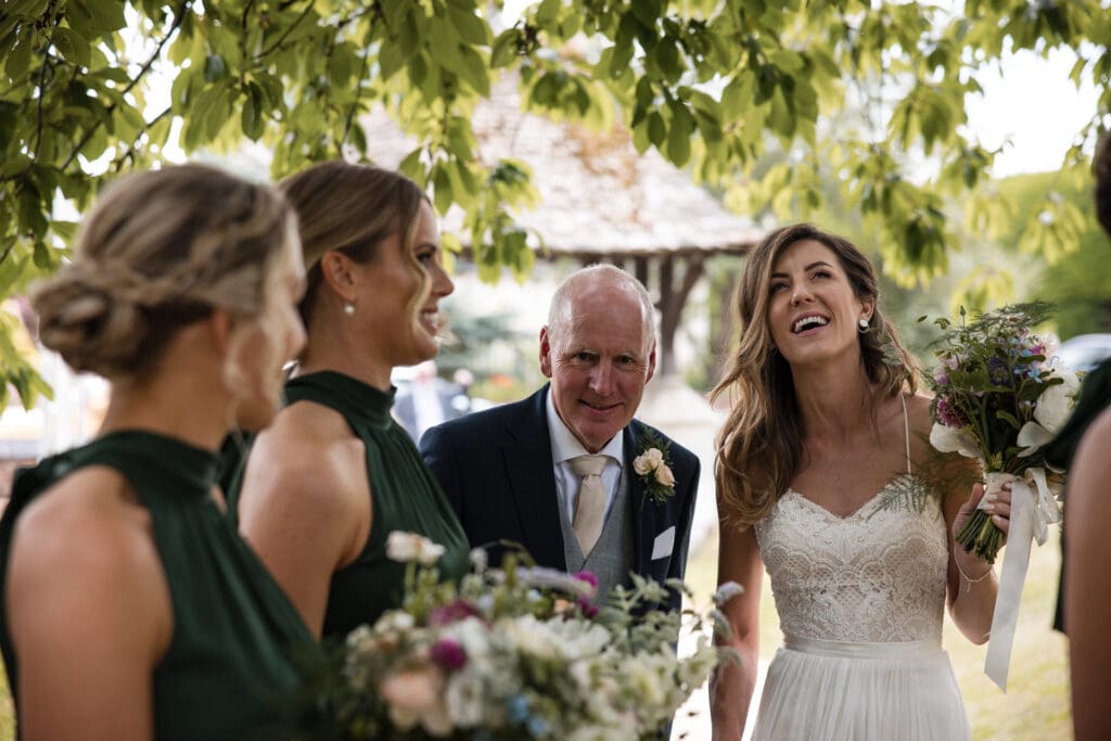 Bride and father talking with Bridesmaids under a tree