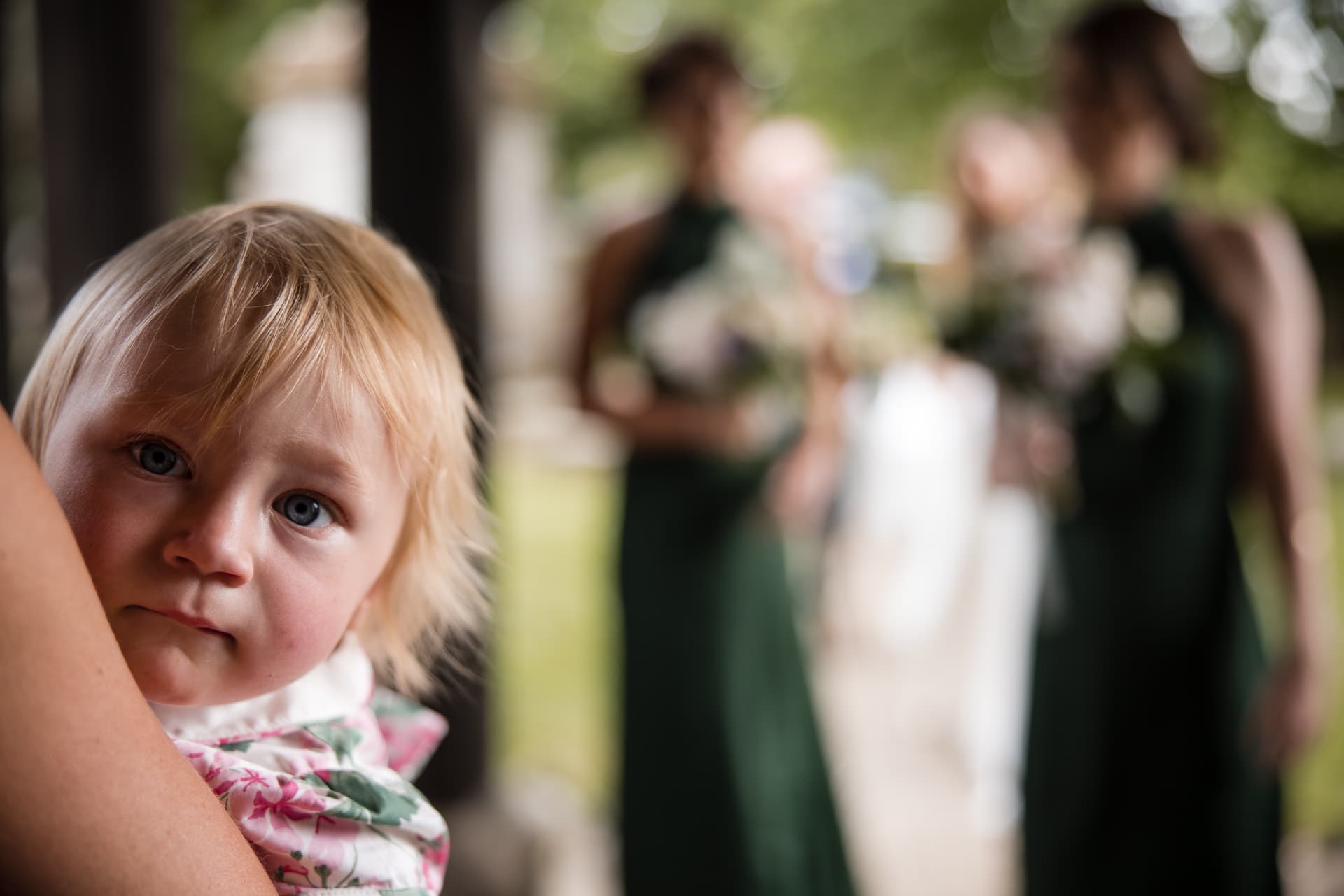 Baby looking at the camera with Bridesmaids out of focus in the background at the Cotswold Sandhurst Wedding
