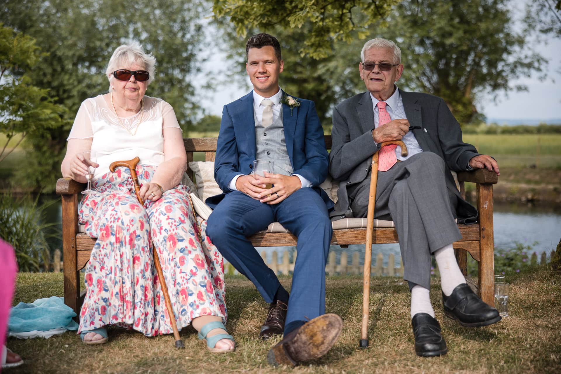 Groom and Grand Parents sat on bench in the garden during the Sandhurst Farm Wedding Reception