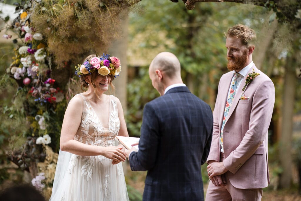 Bride laughing whilst groom reads during outdoor wedding at the Endeavour Woodland wedding venue