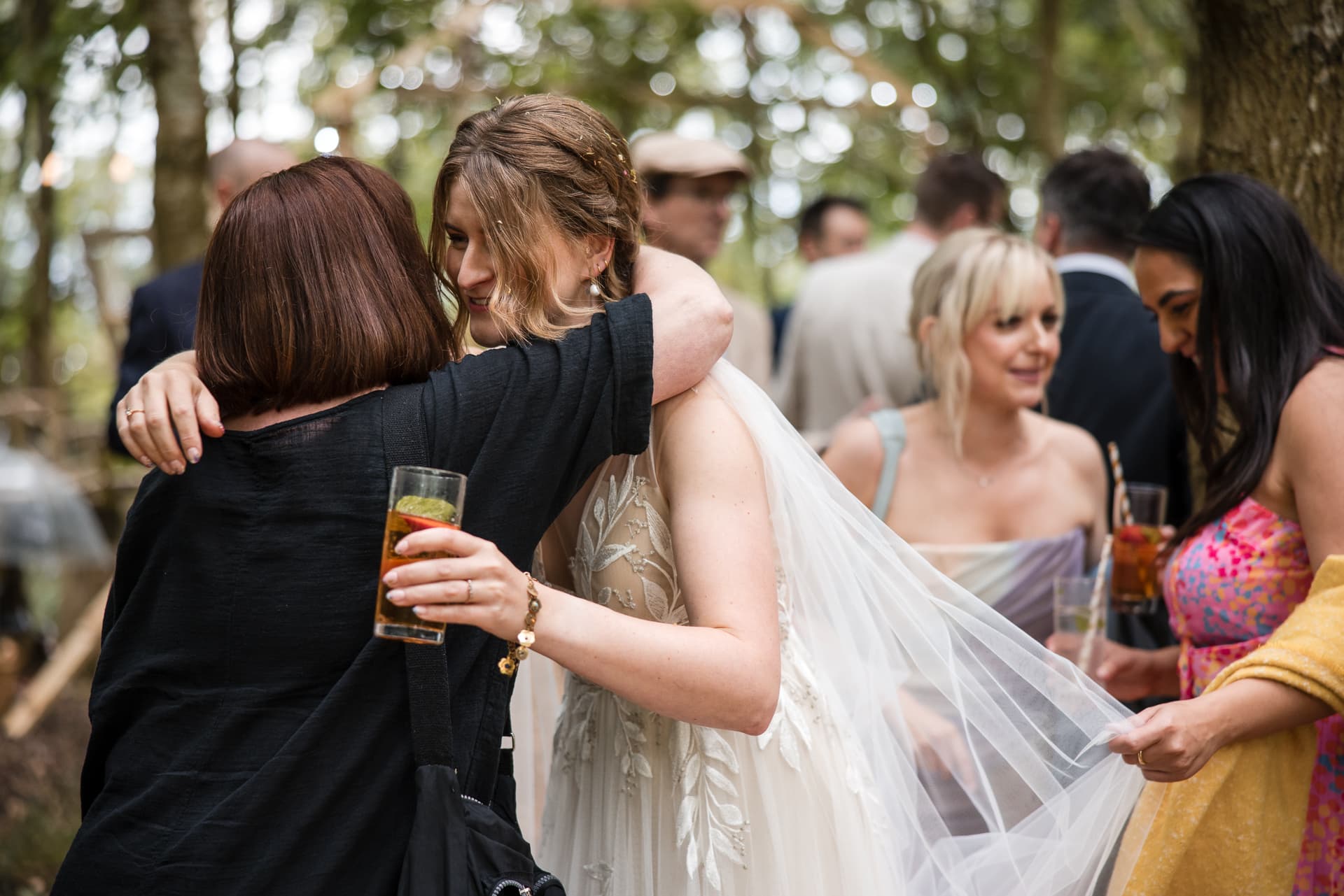 Bride having a cuddle with friend whilst other friends admire her dress at the Endeavour Woodland wedding venue