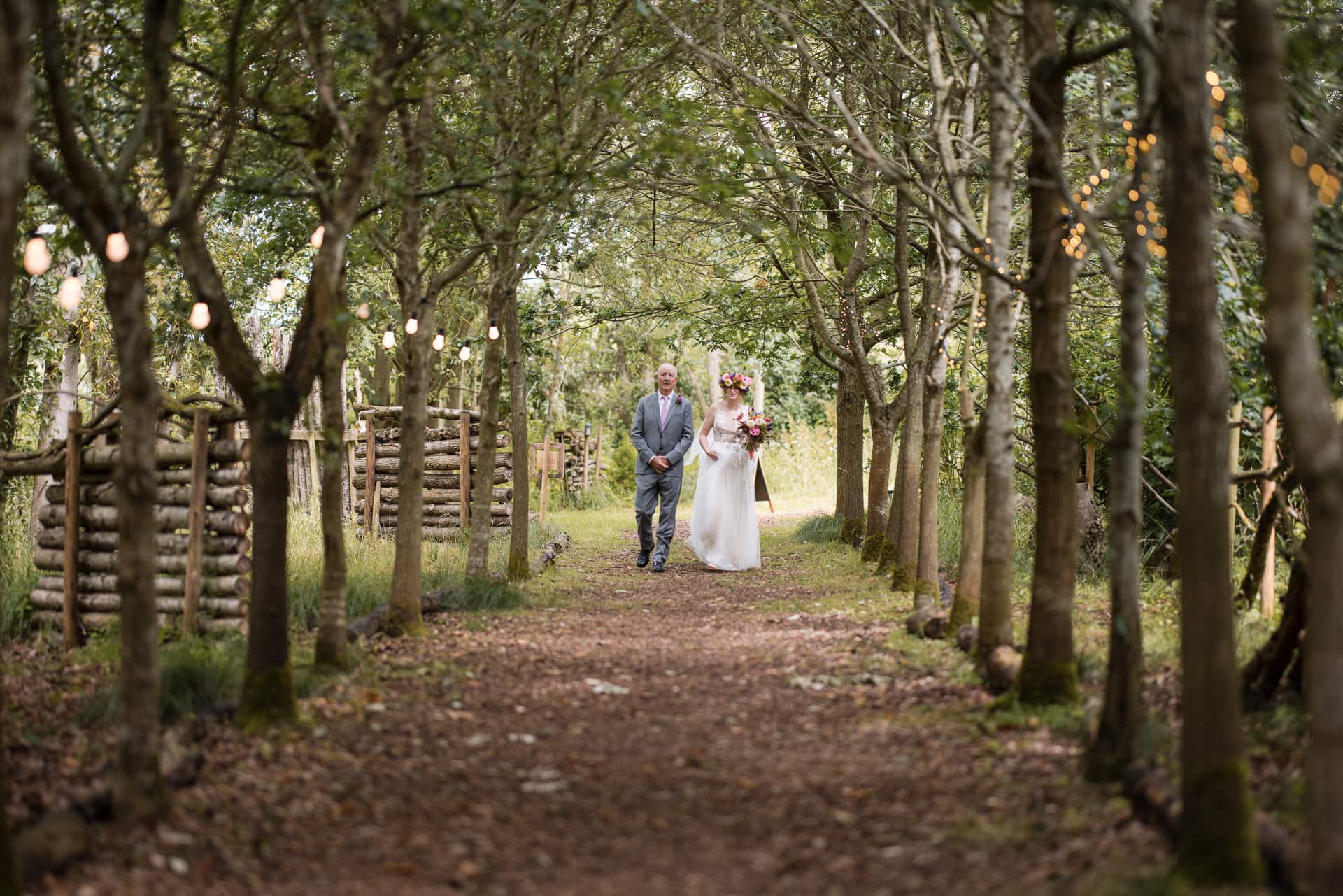 Bride and Father about to walk down a wood lined avenue at the outdoor woodland wedding.