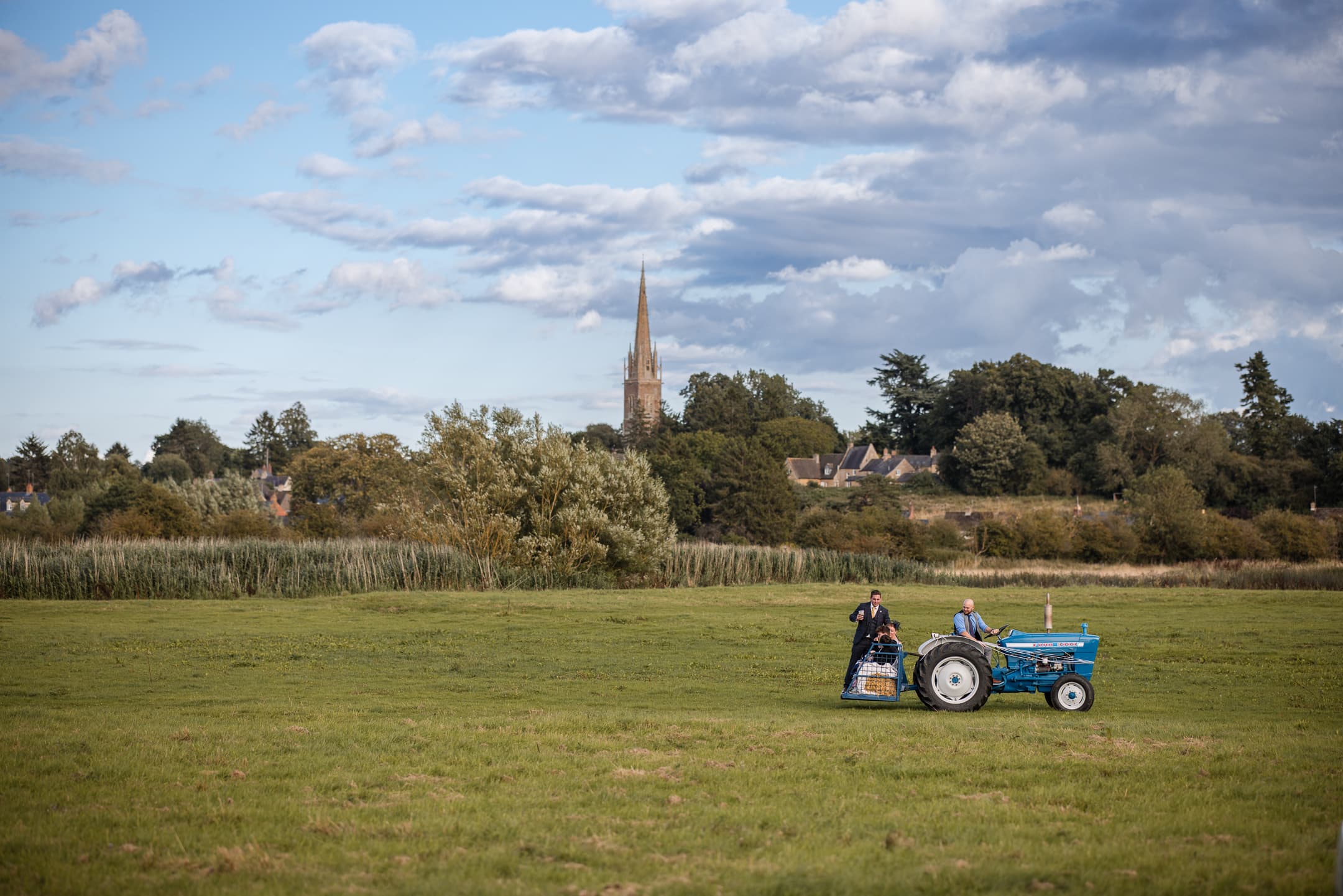Testing out the tractor with guests at Dovecote Barn Wedding, with King Sutton Church Spire in the background