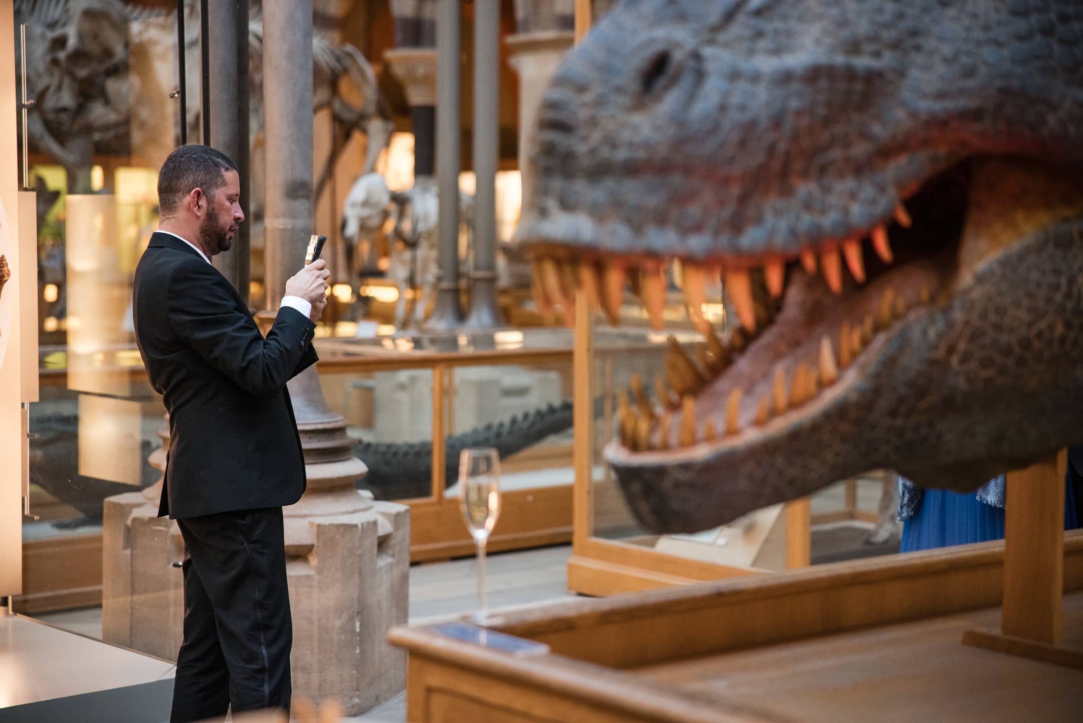 Guest on phone with dinosaur looking on, at the Oxford Natural History Museum wedding reception