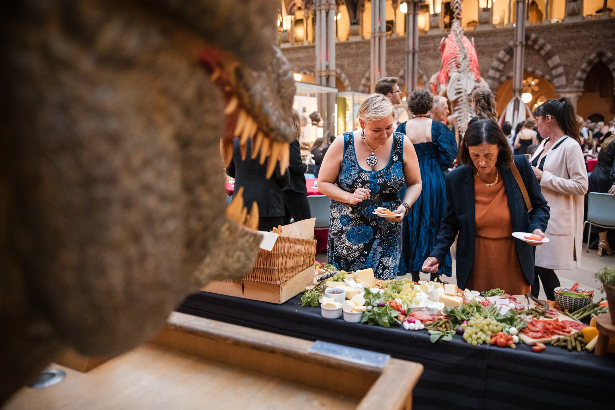 Two guests selecting their food whilst being overlooked by a T-Rex at the Oxford Natural History Museum Wedding reception